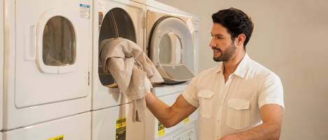 A person in a white shirt loading a laundry basket into a front-loading washing machine.