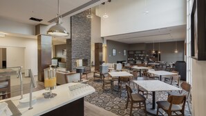 A modern dining area with tables and chairs, a juice dispenser, and a counter with plates and glasses. - Staybridge Suites Silao by IHG (Silao)