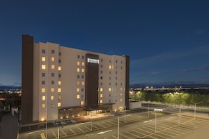A multi-story hotel with a prominent 'Staybridge' sign, a parking lot, and a view of the cityscape in the background. - Staybridge Suites Silao by IHG (Silao)