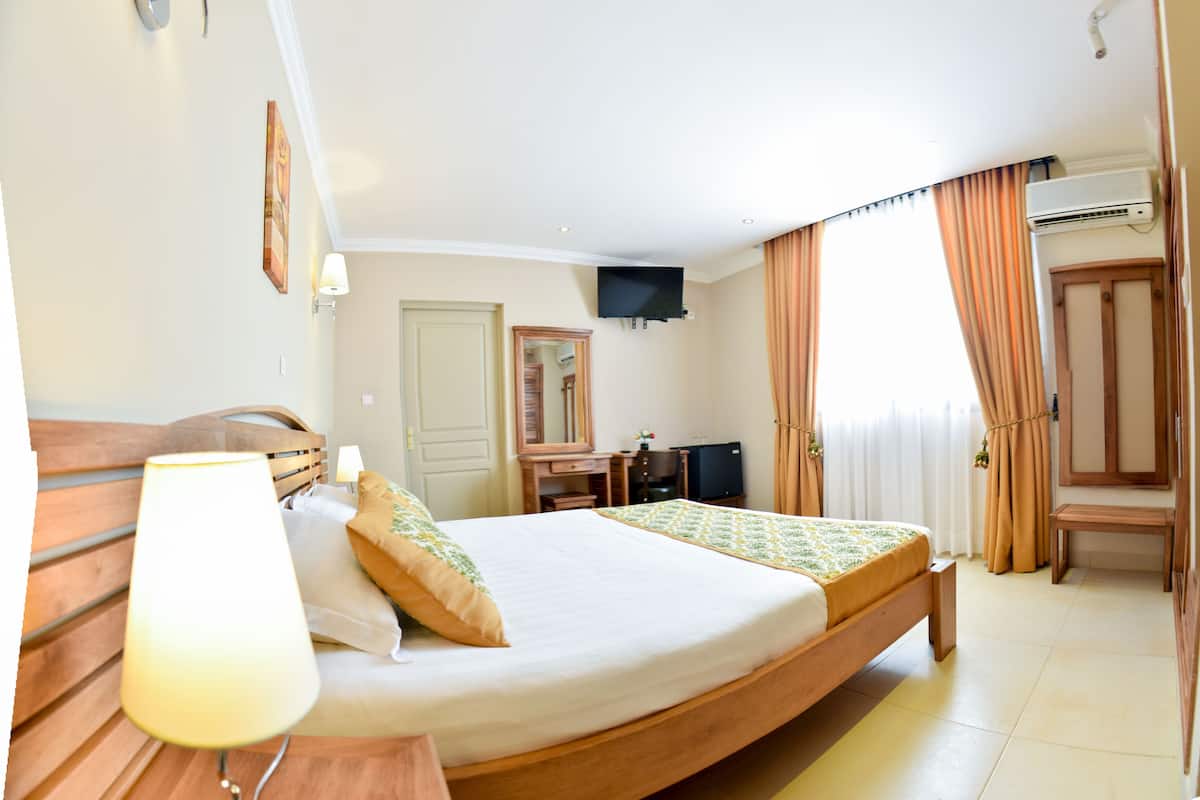 A hotel room with a bed, bedside table, lamp, TV, desk, and curtains.