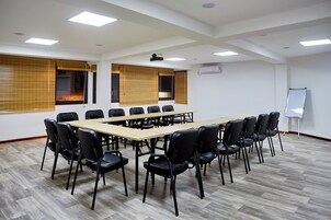 Un salón de conferencias con una larga mesa y sillas, ventanas amplias con persianas y una pizarra.