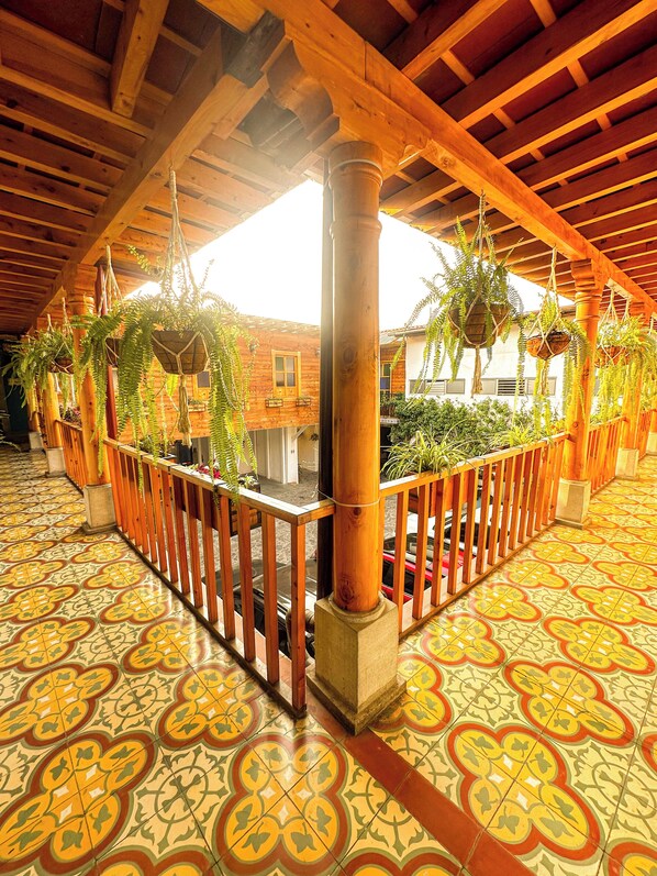 A covered walkway with wooden beams and a tiled floor, featuring hanging planters and a wooden railing.