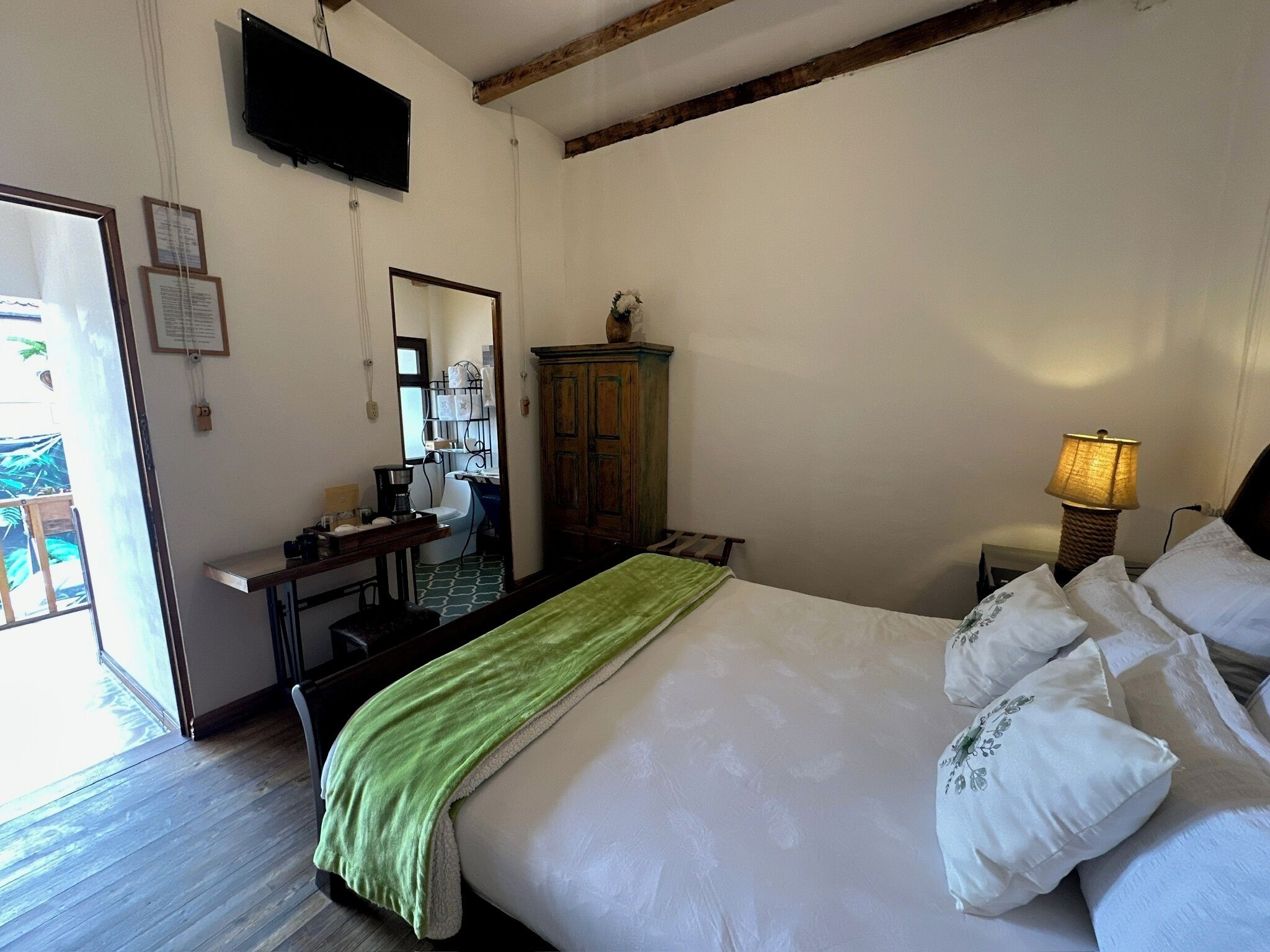 Un dormitorio con una cama, una lámpara de noche, un armario de madera, un televisor y un espejo.