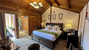 Ein Zimmer aus Holz mit einem Bett, Nachttischen und einer Chandelier. Eine Tür führt in einen Außenbereich.