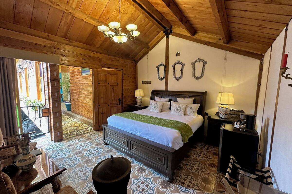 Une pièce en bois avec un lit, des tables de chevet et un lustre. Une porte donne accès à un espace extérieur.