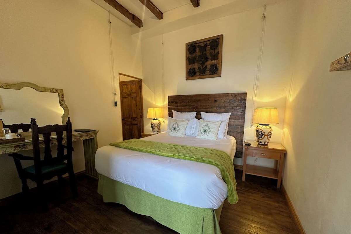 Une chambre à coucher avec un lit en bois, deux tables de chevet avec des lampes, une chaise en bois, un bureau et une porte en bois.