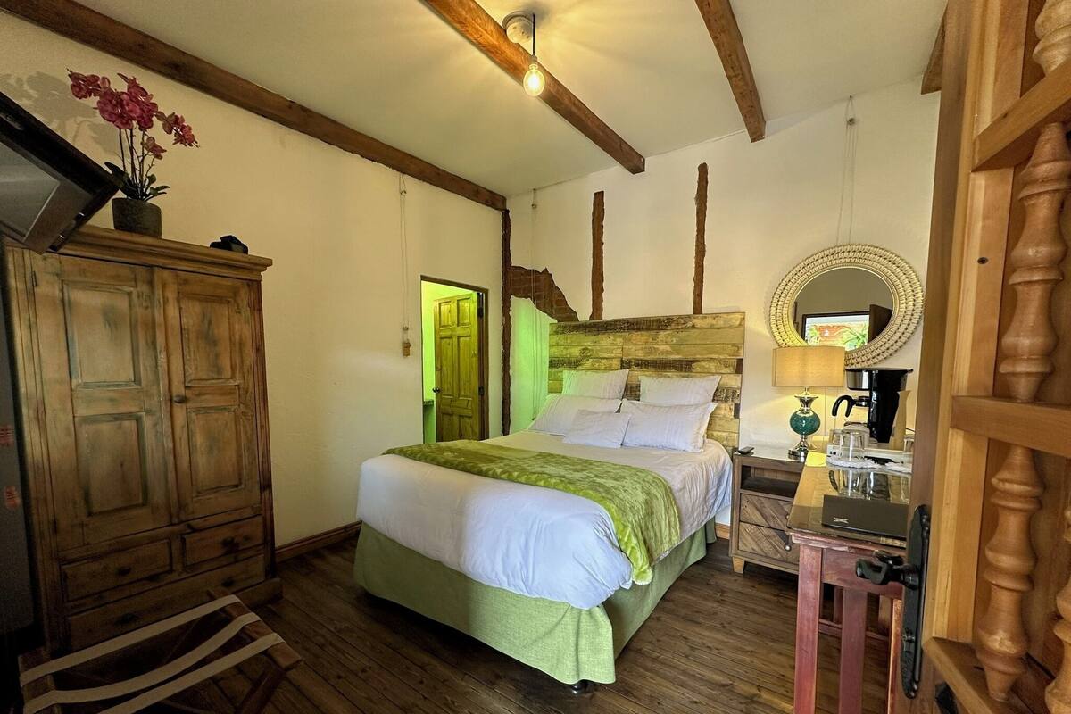 Une chambre à coucher avec un lit en bois, une armoire en bois, un miroir et une petite table avec une lampe.