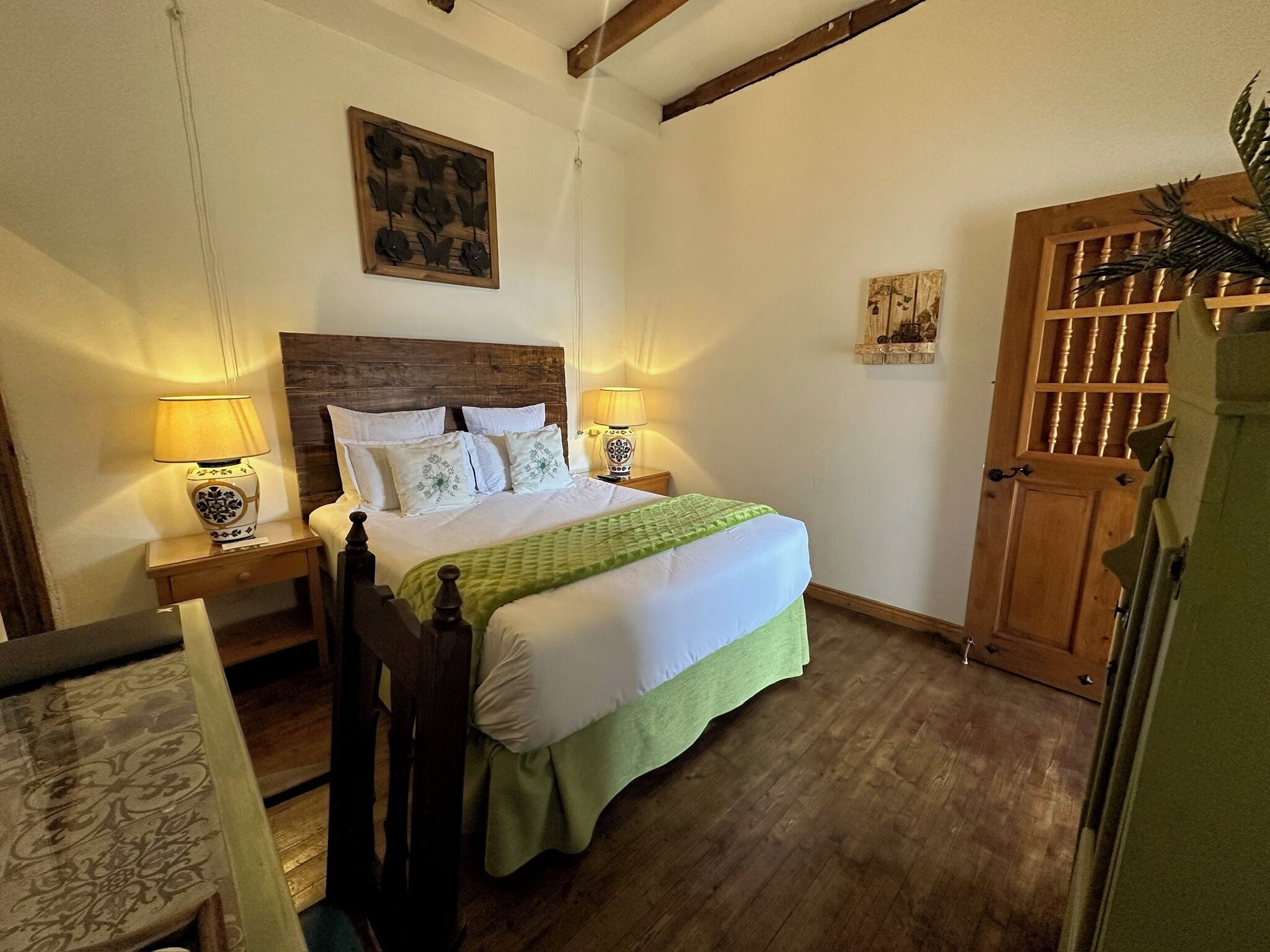 Quarto com cama de madeira, duas mesas de cabeceira com luminárias, uma porta de madeira e uma pequena obra de arte na parede acima da cama.