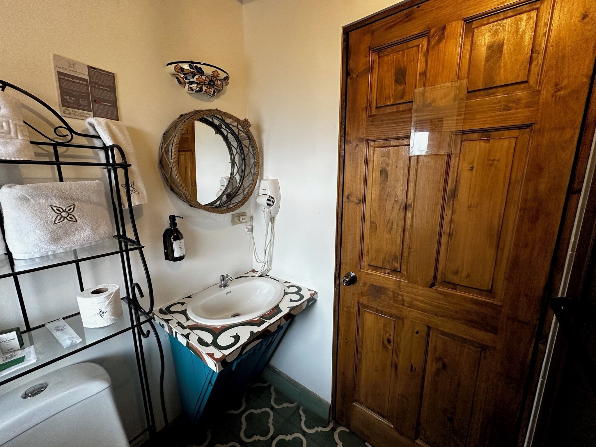 A bathroom with a wooden door, a white sink, a mirror, a towel rack, and a patterned floor.