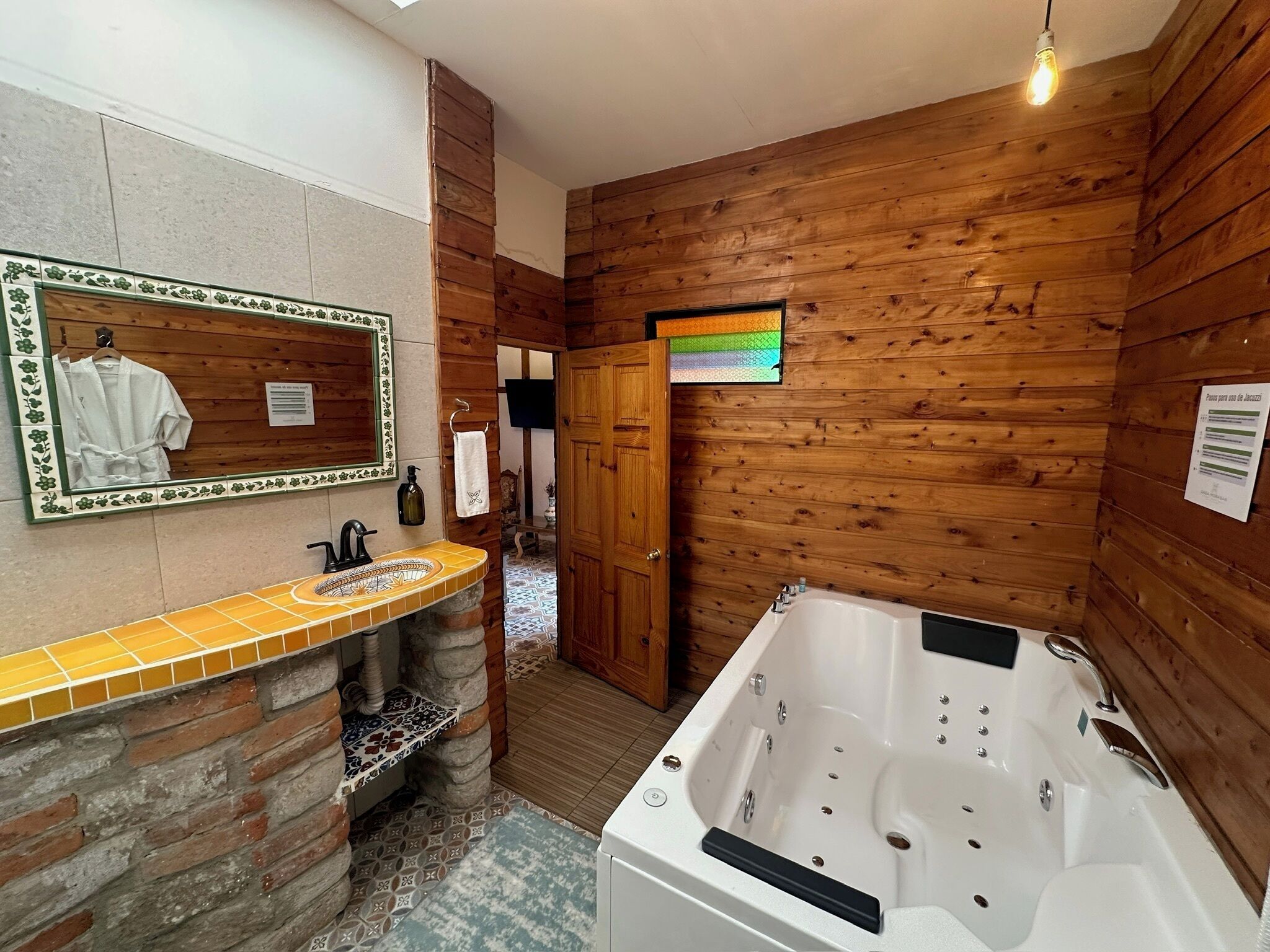 A bathroom with a wooden interior, a tiled sink, a large bathtub, and a mirror with a floral frame.
