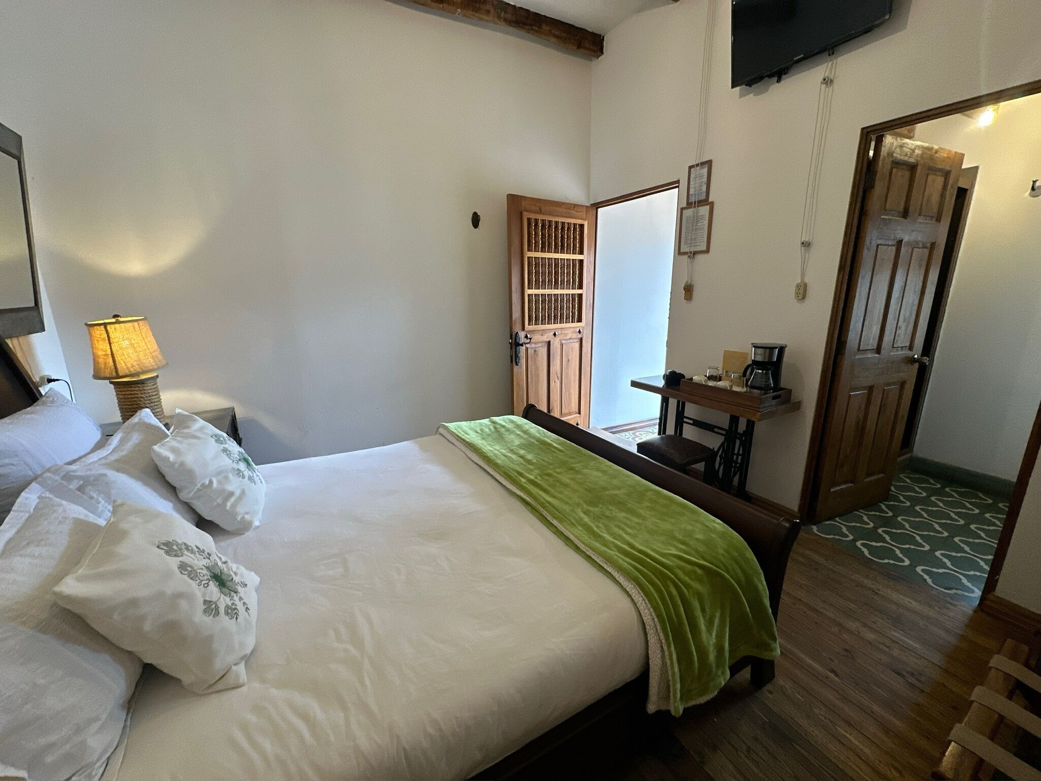 A hotel room with a bed, a desk, a chair, a lamp, and a television.
