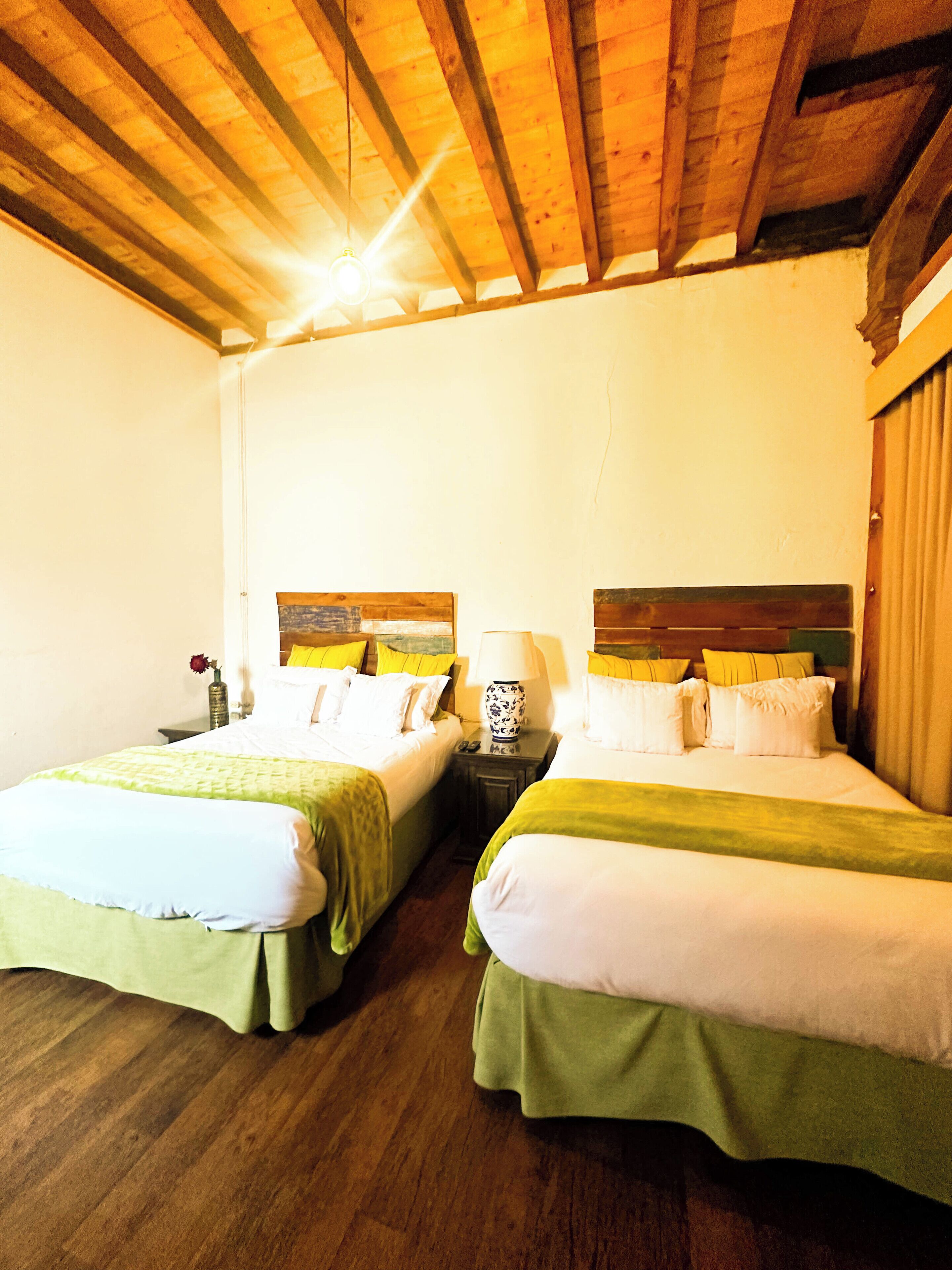 Una habitación con dos camas, vigas de madera en el techo y una mesita de noche con lámpara entre las camas.