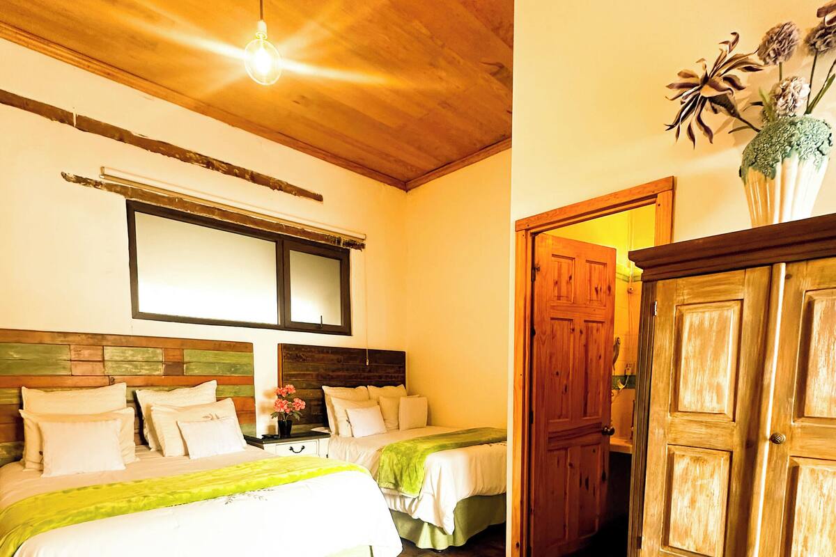 Une chambre avec deux lits, un plancher en bois, un grand miroir et une armoire en bois.