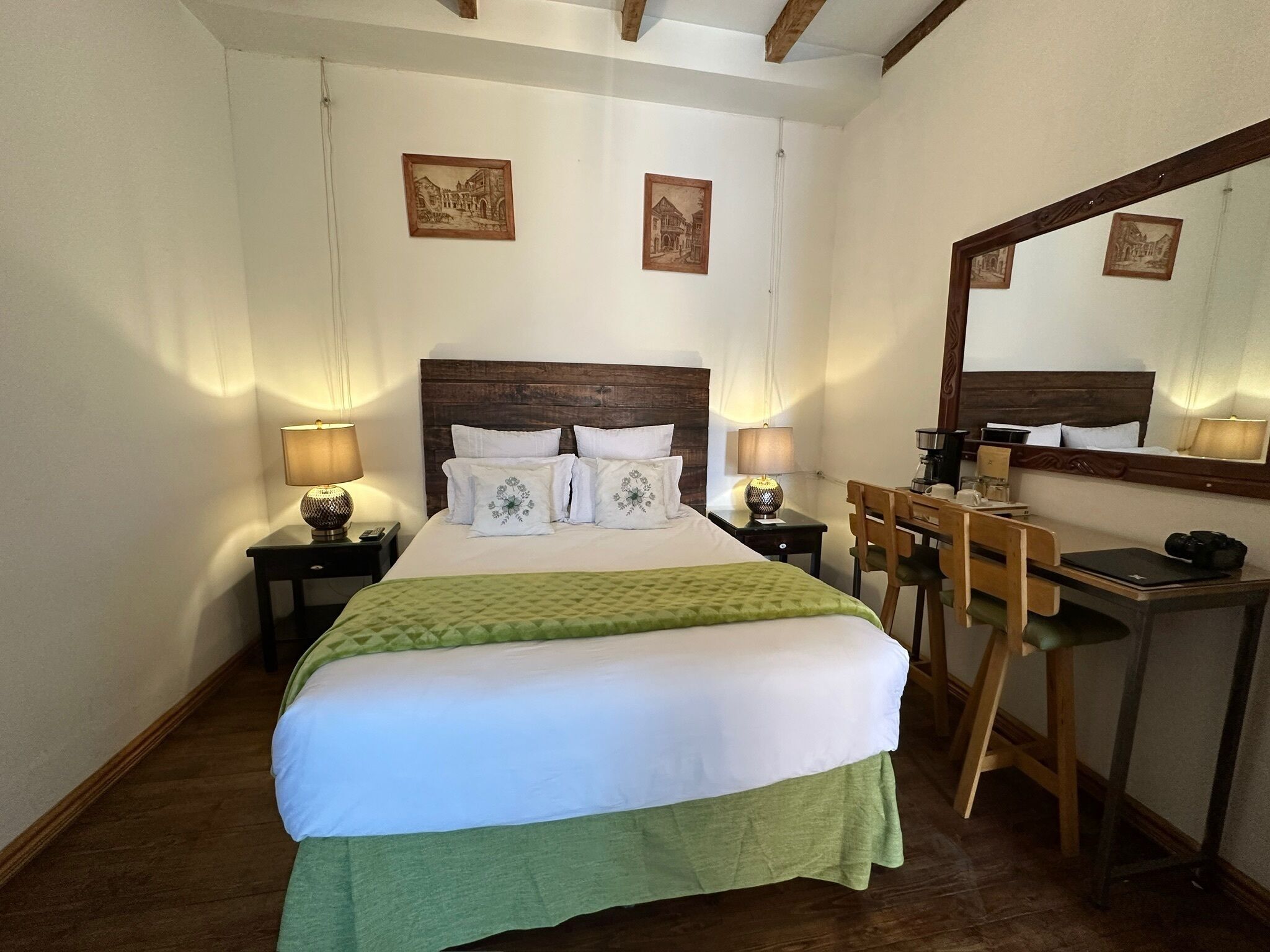 Ein Hotelzimmer mit einem großen Bett, zwei Nachttischen mit Lampen, einem Schreibtisch mit Stuhl und einem Spiegel an der Wand.