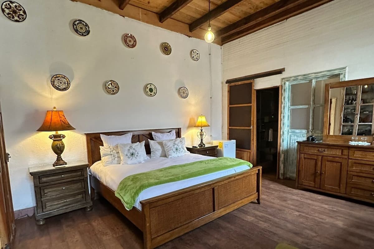 Une chambre à coucher avec un lit en bois, deux tables de chevet avec des lampes, un canapé vert et une armoire en bois.