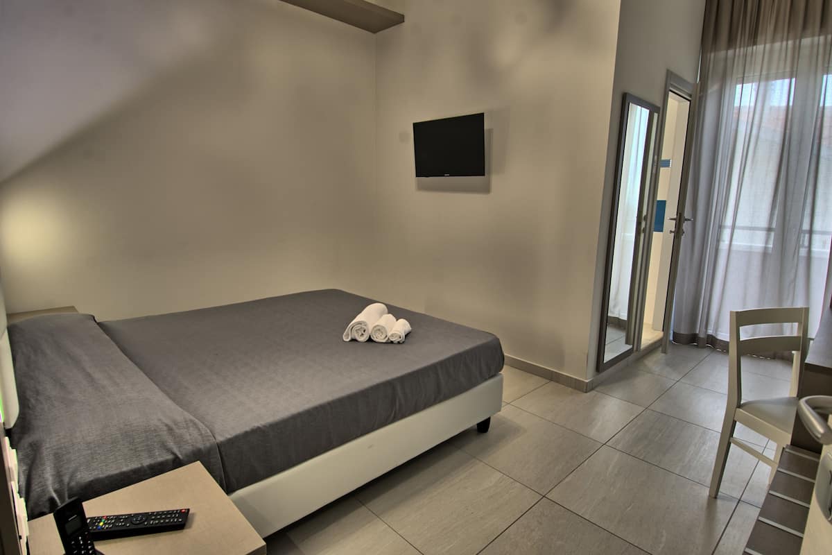 Ein Hotelzimmer mit Bett, Flachbildfernseher an der Wand, einem Sessel und einer Tür zu einem Balkon.