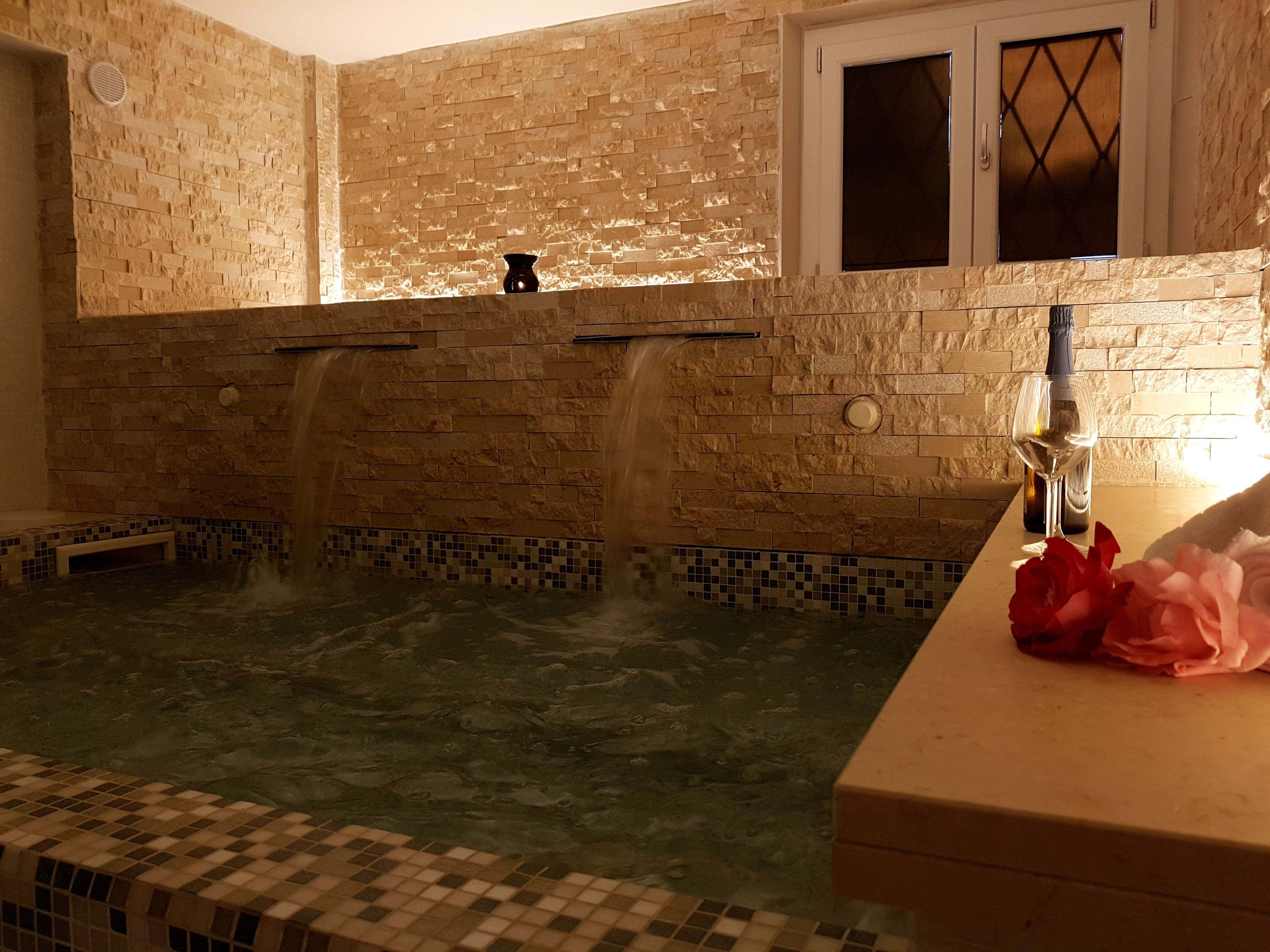 Un área de spa con pared de piedra, una ventana y una botella de vino sobre una encimera.