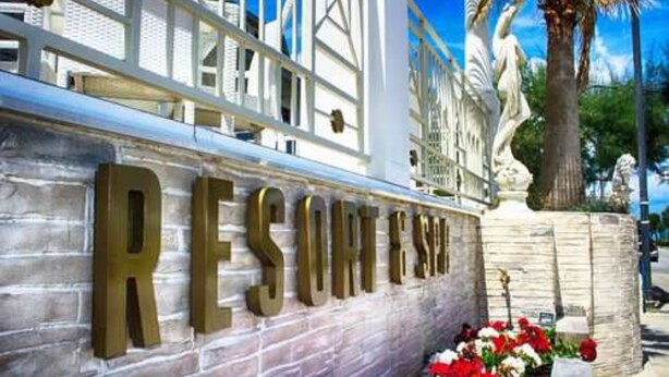 Façana d'edifici amb les paraules "RESORT" i "ISLAND" en lletres grans, una estàtua i una palmera.
