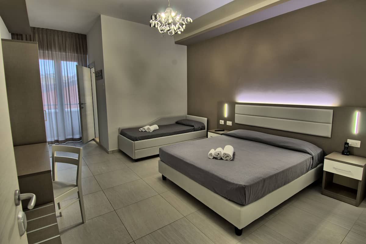 Ein modernes Hotelzimmer mit einem großen Bett, einem kleineren Bett, einem Schreibtisch und einem Sessel.