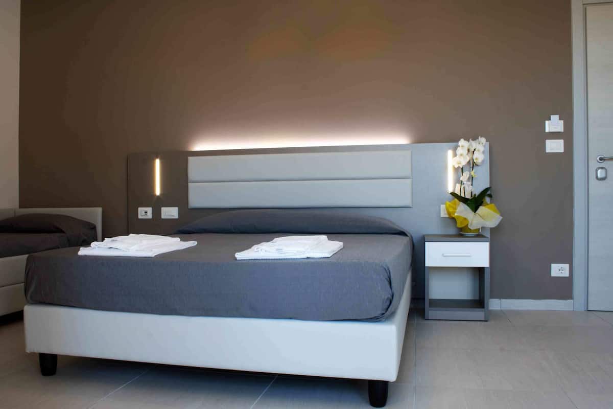 Ein modernes Schlafzimmer mit einem großen Bett, Nachttischen, einem Beistelltisch und einer Wandleuchte.