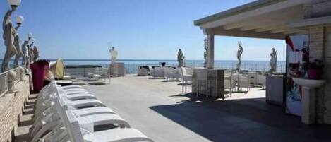 A rooftop terrace with white lounge chairs, a covered seating area, and a view of the sea.
