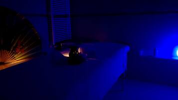 A dimly lit room with a bed, a bedside table, and a wall-mounted shelf.