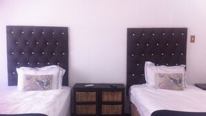 Une chambre d’hôtel avec deux lits, chacun doté d’une tête de lit sombre et de draps blancs. Une petite table avec des paniers se trouve entre les lits.