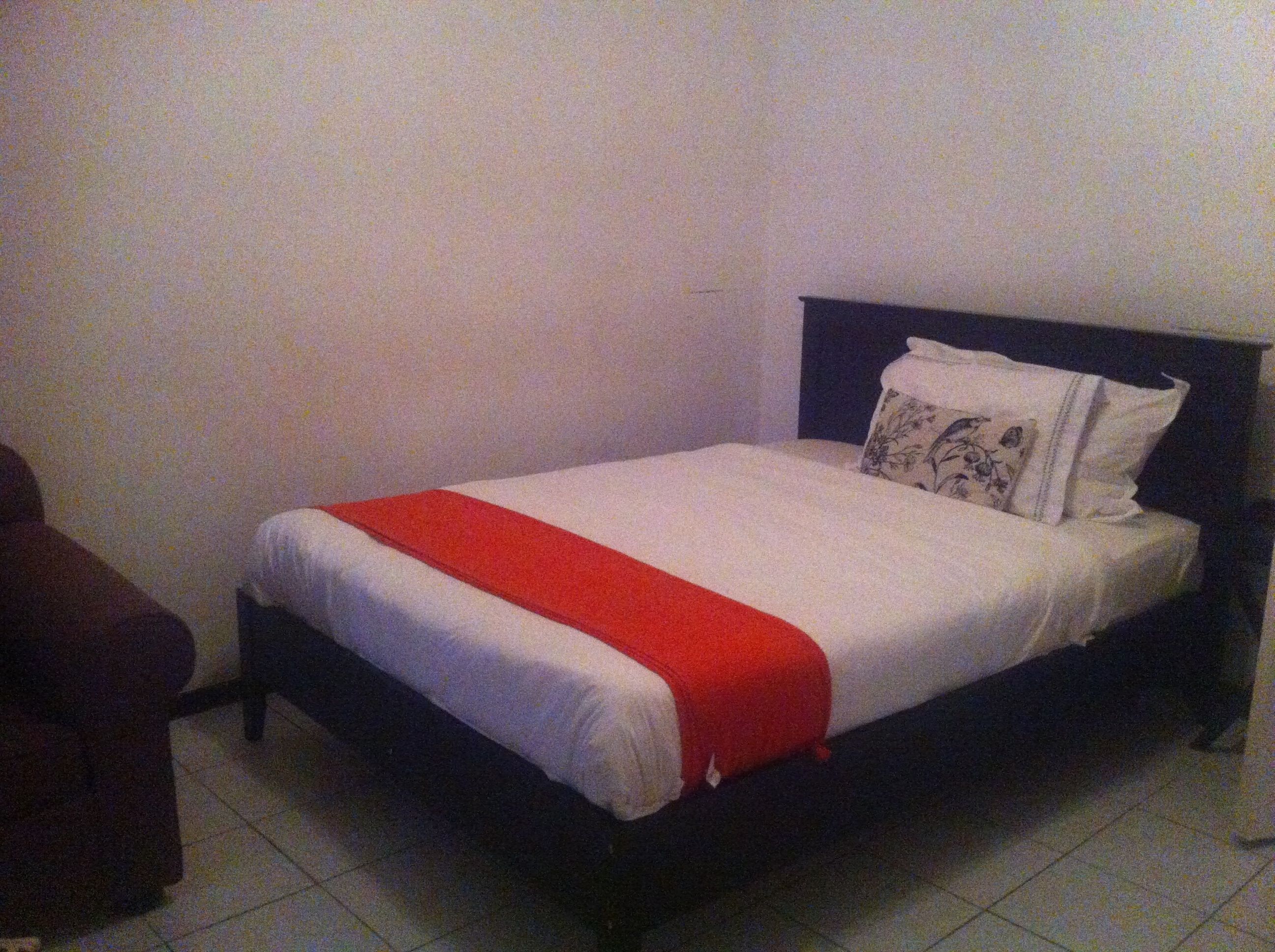 A single bed with a white and red bedspread, a dark headboard, and two pillows with floral designs.