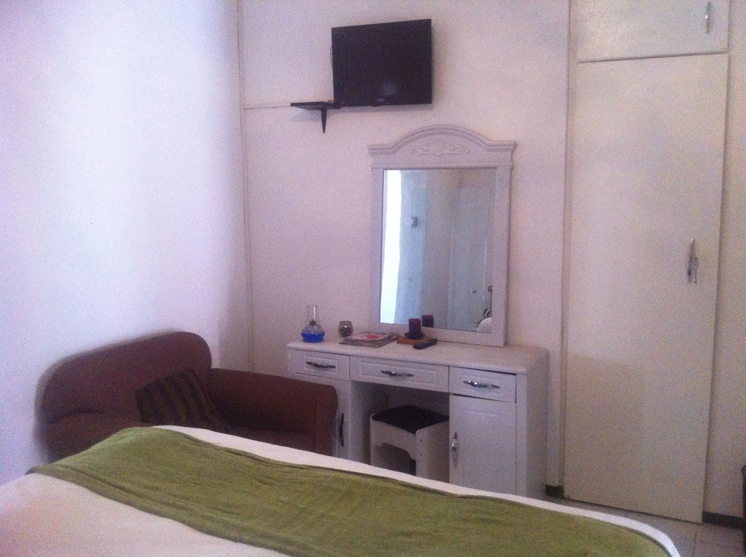 Ein Schlafzimmer mit einem Bett, einem Schminktisch, einem Spiegel, einem Fernseher und einem Kleiderschrank.