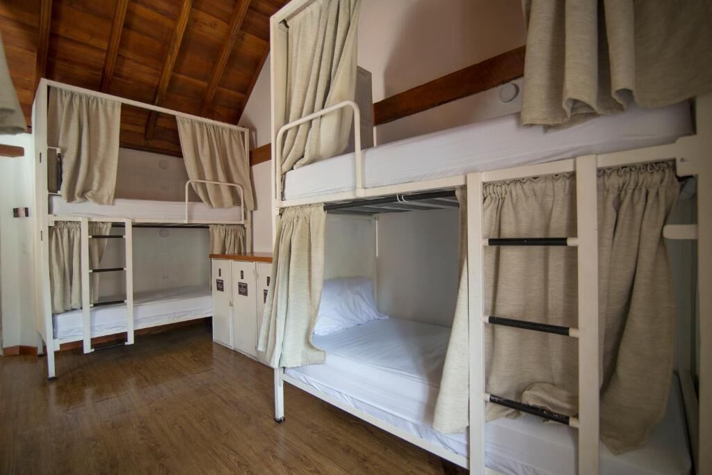 A room with bunk beds, wooden floors, and curtains.