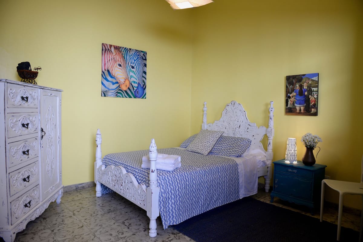 A bedroom with a bed, a dresser, two paintings, and a nightstand.