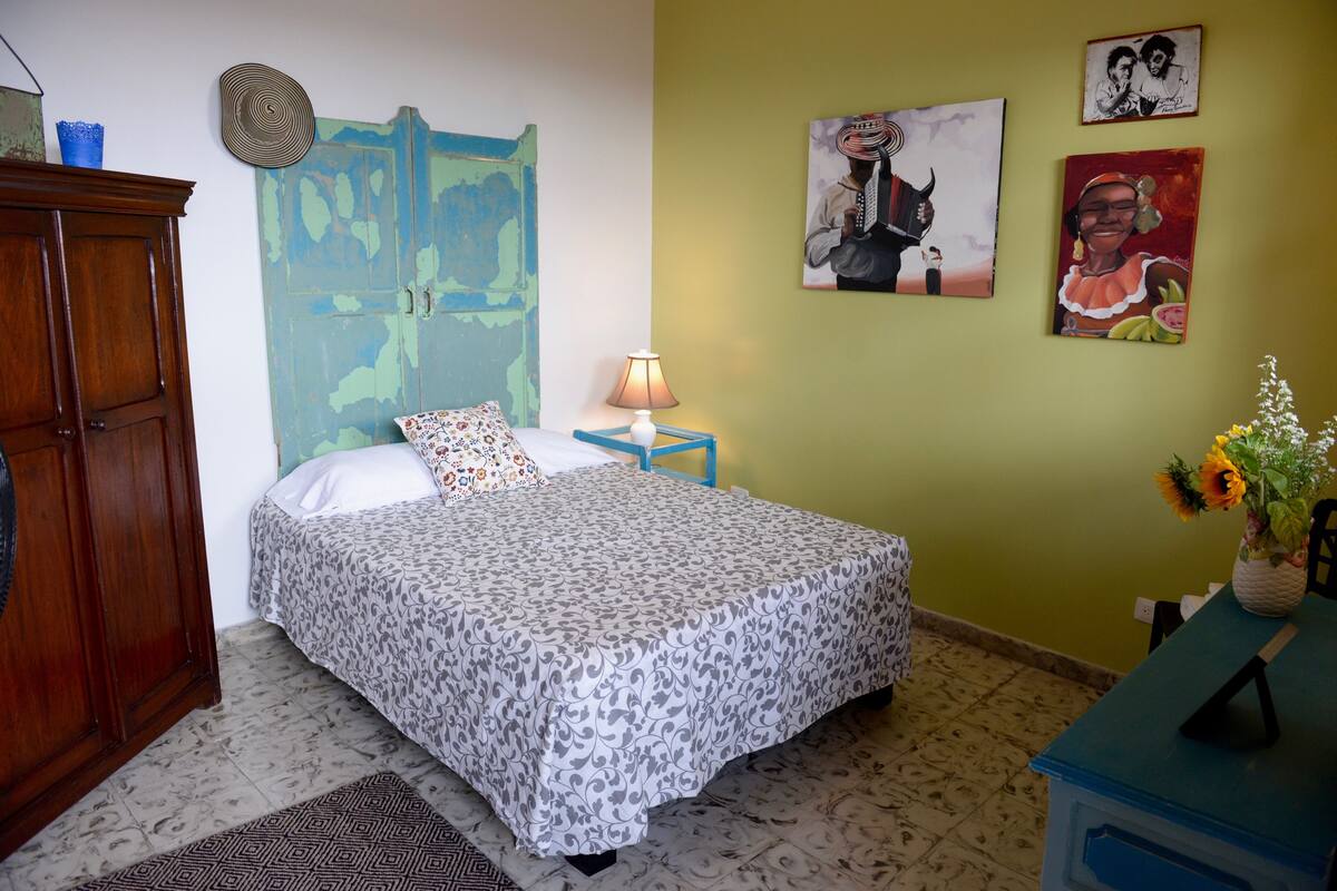 A bedroom with a bed, a nightstand, a lamp, a dresser, and wall art.