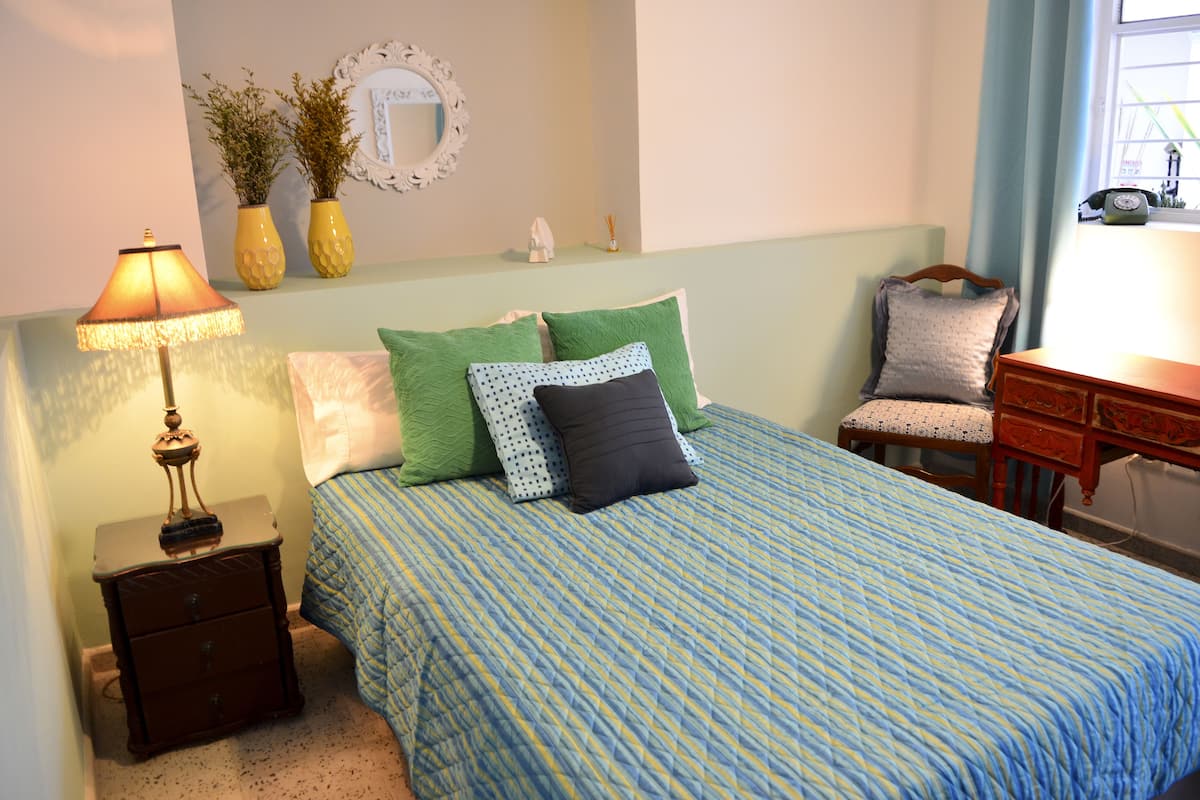 A bedroom with a bed, nightstand, lamp, dresser, chair, and a window with curtains.