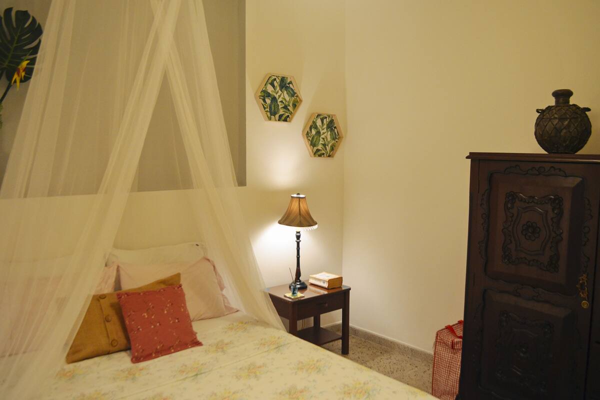 A bedroom with a canopy bed, a bedside table with a lamp, and a wooden cabinet.