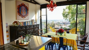 A kitchen with a large window, a dining area with a yellow tablecloth, and a view of a cityscape. - Magic Garden House (Cali)