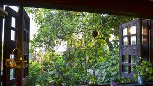 A window with a view of lush greenery and a rustic building. - Magic Garden House (Cali)