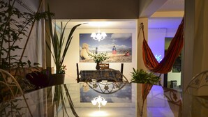 A room with a glass table reflecting a painting, a hanging chair, and potted plants. - Magic Garden House (Cali)