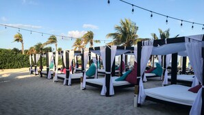 A row of beachside cabanas with white canopies and colorful cushions, set against a backdrop of palm trees and a clear sky. - Hotel Select Inn Quinta Playa del Carmen (Playa del Carmen)