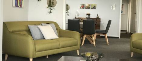 Een woonkamer met een groene bank, een houten salontafel, en een eethoek met een tafel en stoelen.