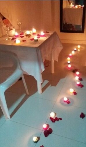 Una mesa de comedor con velas y pétalos de rosa sobre el suelo.