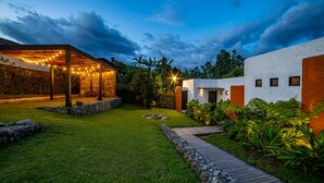 A modern outdoor patio area with a stone wall, a wooden deck, and a well-lit pergola. - Salento Pequeño Hotel (Salento)