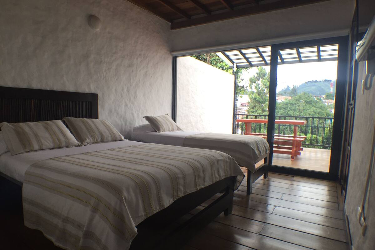 Ein Schlafzimmer mit zwei Betten, Holzboden und einem Balkon mit Blick auf Grünflächen.