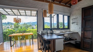 A kitchen with a large window, wooden flooring, and a dining area with yellow chairs. - Salento Pequeño Hotel (Salento)