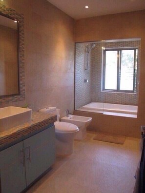 A modern bathroom with a large mirror, a bathtub, a bidet, and a toilet. - Casa Venecia (Playa del Carmen)