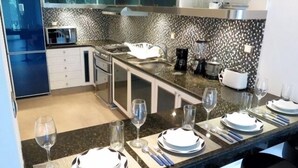 A modern kitchen with granite countertops, stainless steel appliances, and a black and white patterned backsplash. - Casa Venecia (Playa del Carmen)