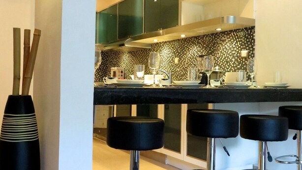 A modern kitchen with a black countertop, stainless steel stools, and a decorative black vase. - Casa Venecia (Playa del Carmen)