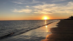 Ein Strand bei Sonnenuntergang, die Sonne tief am Horizont, ihr Spiegelbild im Wasser.