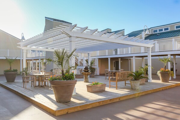 An outdoor patio area with wooden flooring, potted plants, and outdoor furniture.