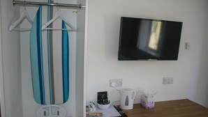 Une salle de bain équipée d’un porte-serviettes, d’une étagère pour la douche, d’un téléviseur fixé au mur, d’un plan de travail en bois et d’une boîte à mouchoirs.
