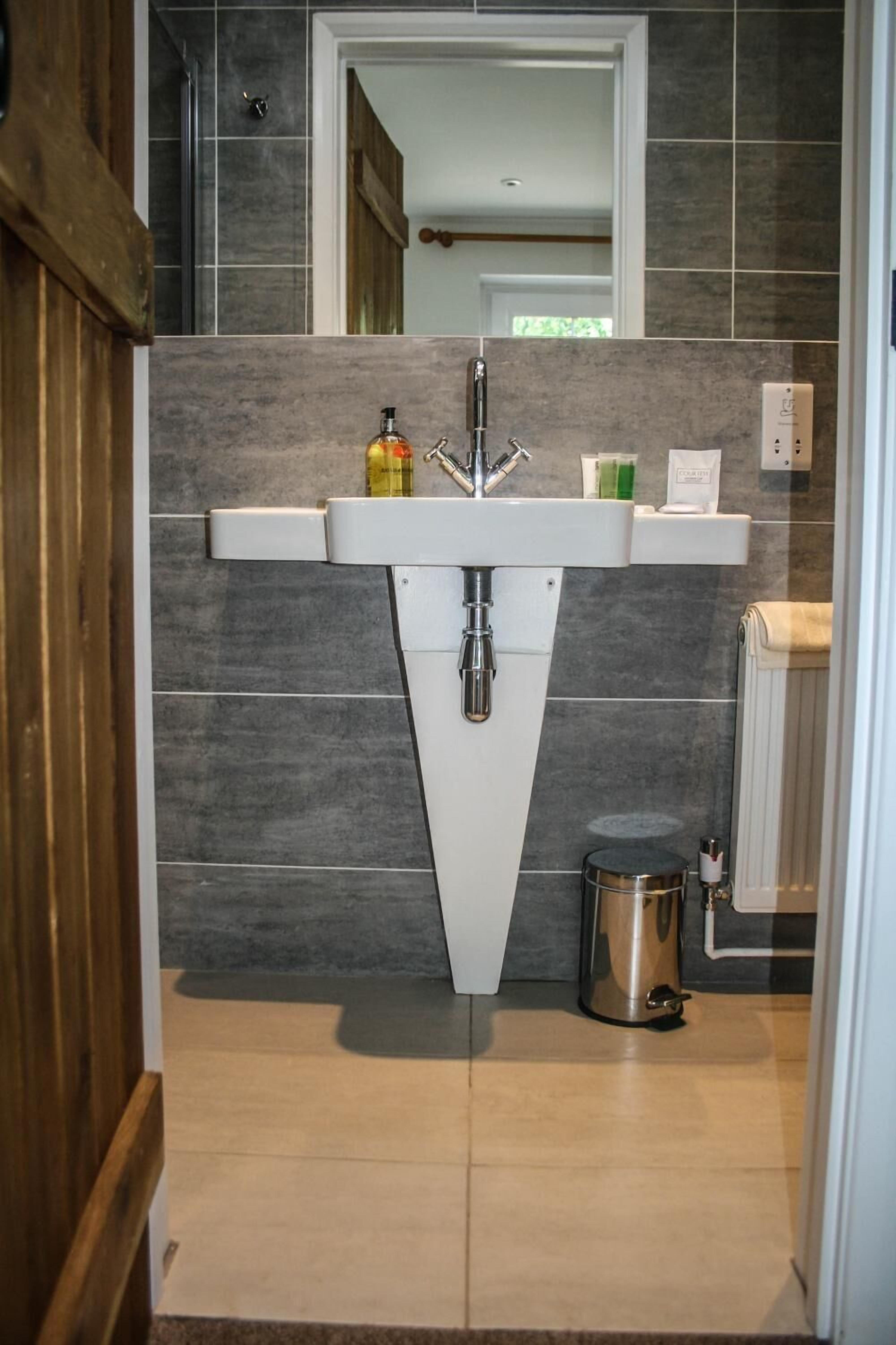 A modern bathroom with a white sink, dark tiled walls, and a visible trash can.